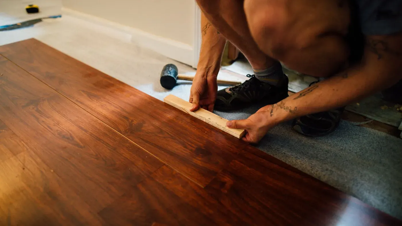 Handwerker verlegt Laminatdielen mit Schlagklotz und Hammer in einer Wohnung